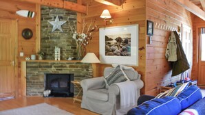 A cozy cabin interior with a stone fireplace, wooden walls, a gray sofa, and a framed picture on the wall.
