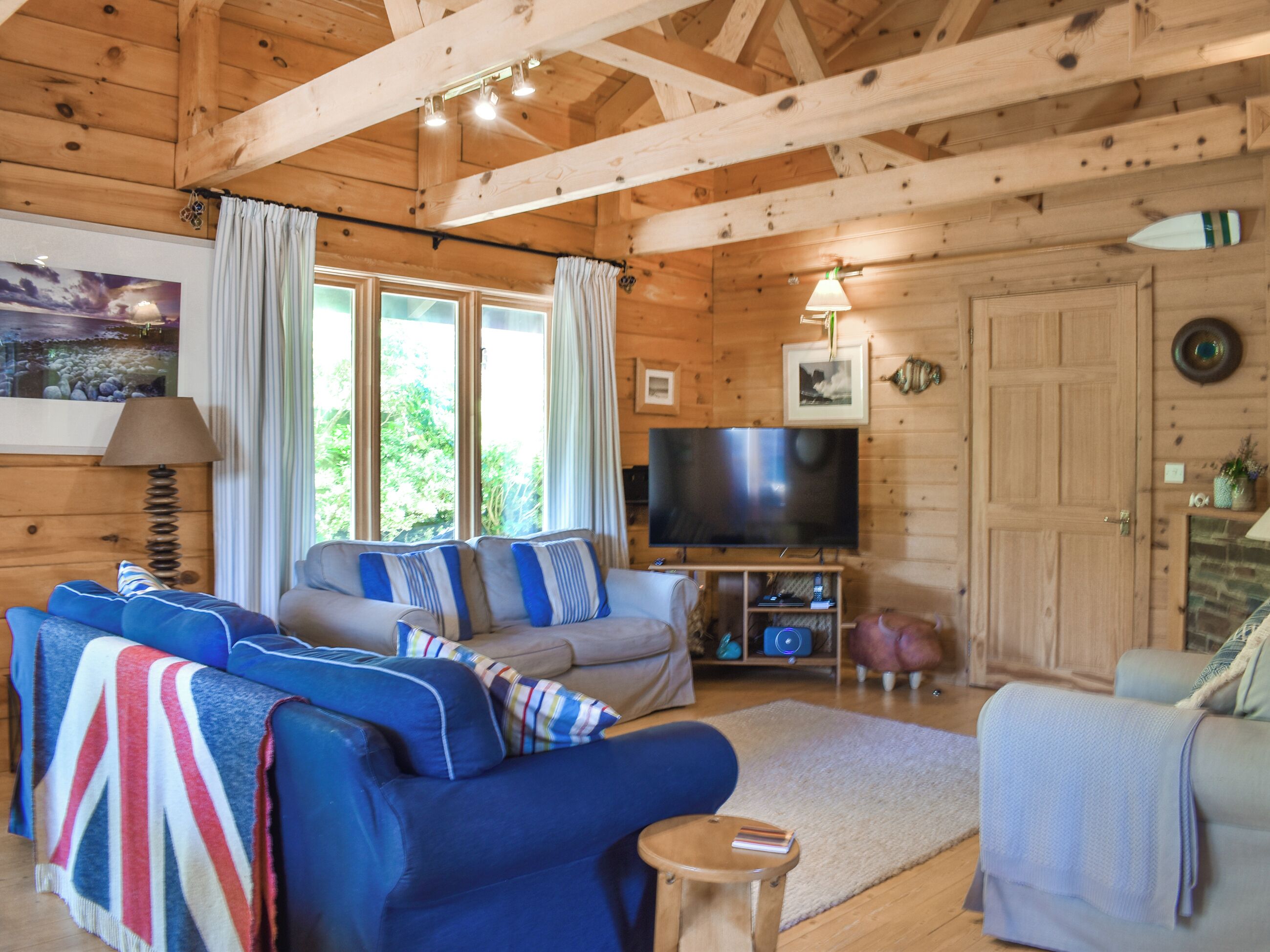A cozy cabin-style living room with a large TV, wooden beams, and a fireplace.