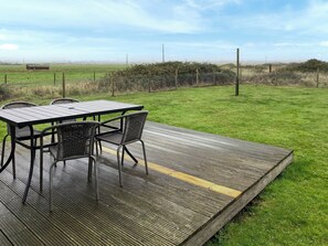 A deck with a table and chairs, surrounded by a grassy field and a fence.