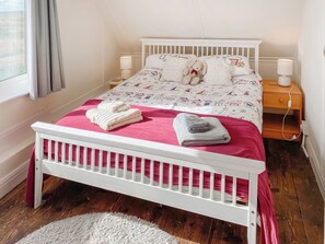 A neatly made bed with a red blanket, two pillows, and a teddy bear. There are two bedside lamps and a wooden nightstand with a lamp.