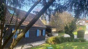 Een houten huis met pannendak en blauwe luiken, omringd door een verzorgd gazon en een haag.