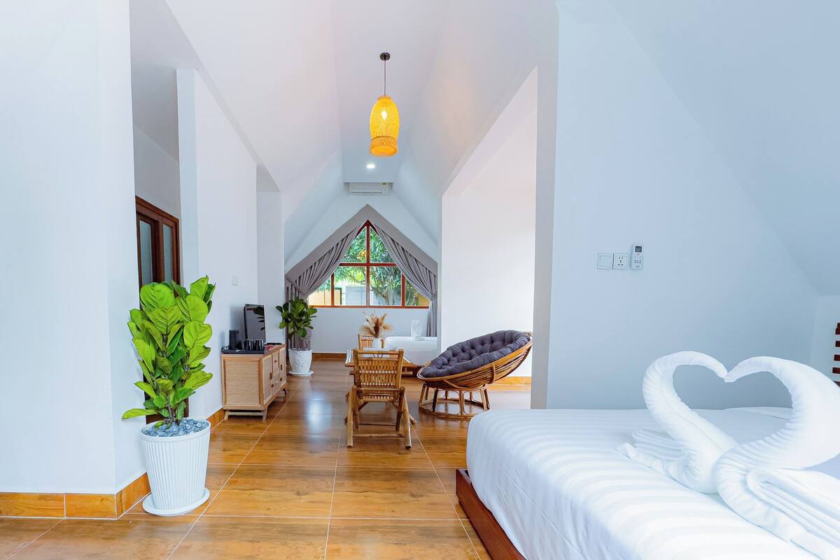 A hotel room with a bed, a dining area, and a view through a window.