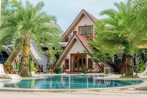Un resort con piscina, palmeras y un edificio de dos pisos con techo rojo.