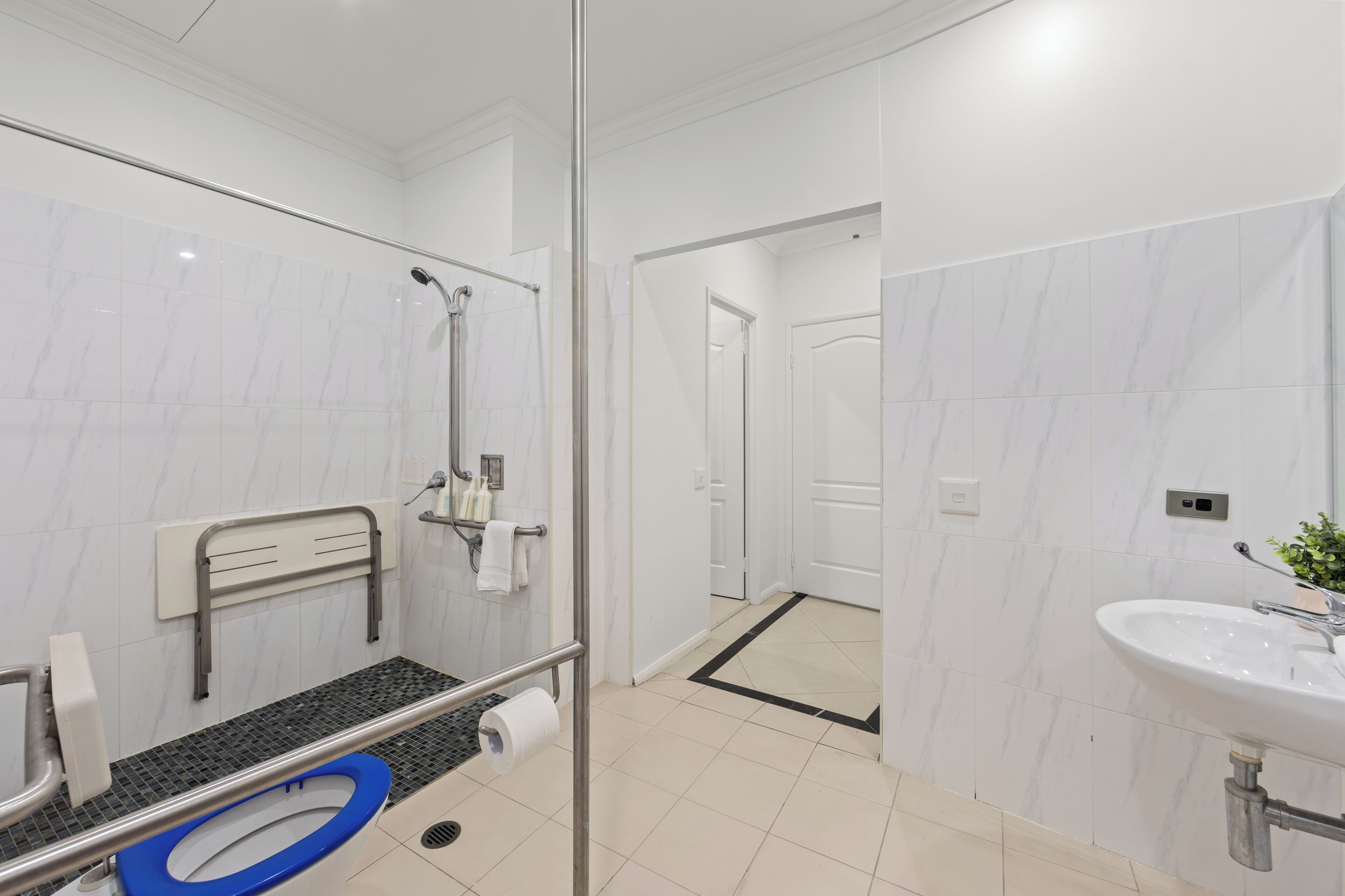 Un baño moderno con cabina de ducha de vidrio, un inodoro con asiento azul y un lavabo con espejo.