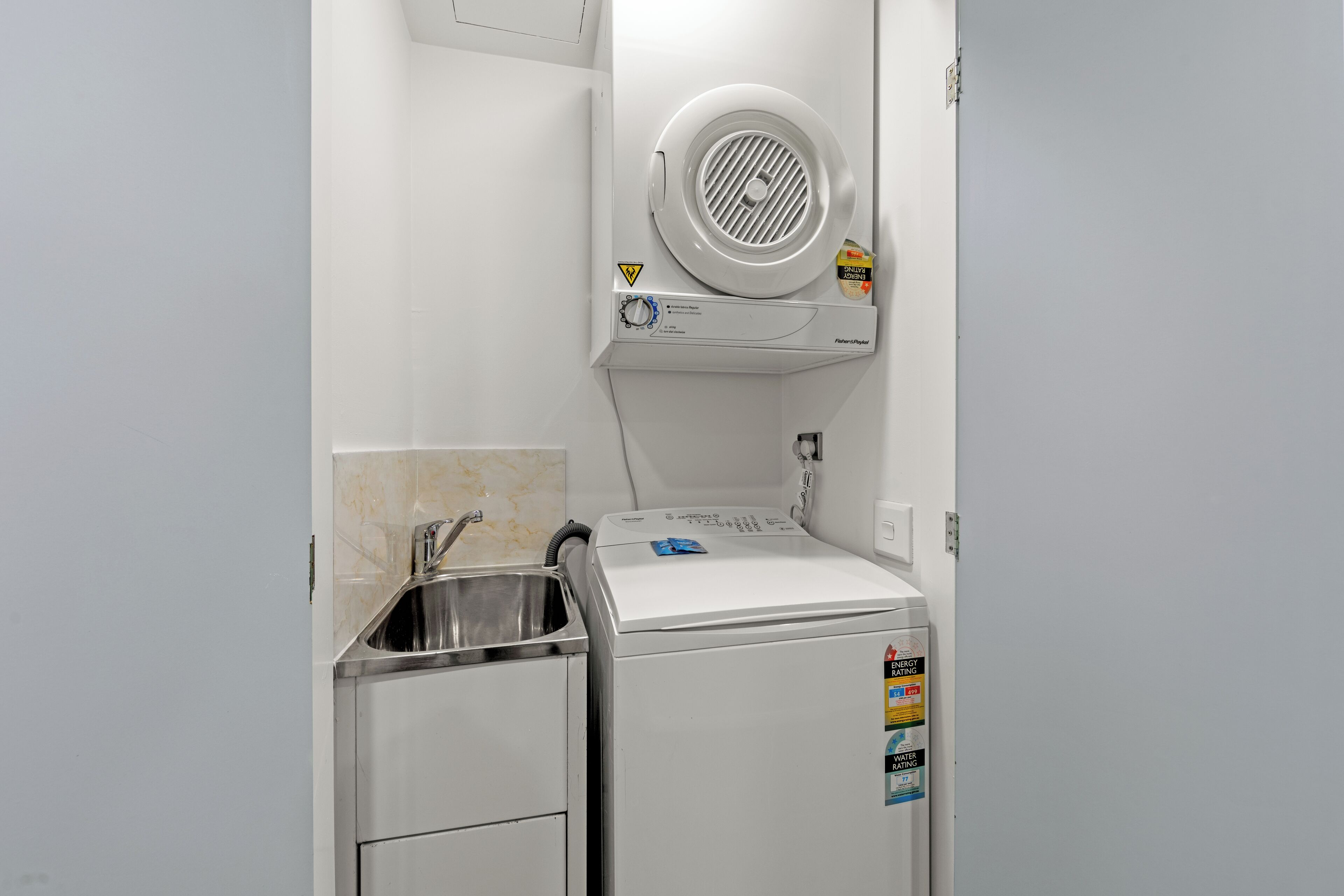Une petite buanderie équipée d’un lave-linge et d’un sèche-linge intégrés, d’un évier en acier inoxydable et d’un dosseret carrelé.