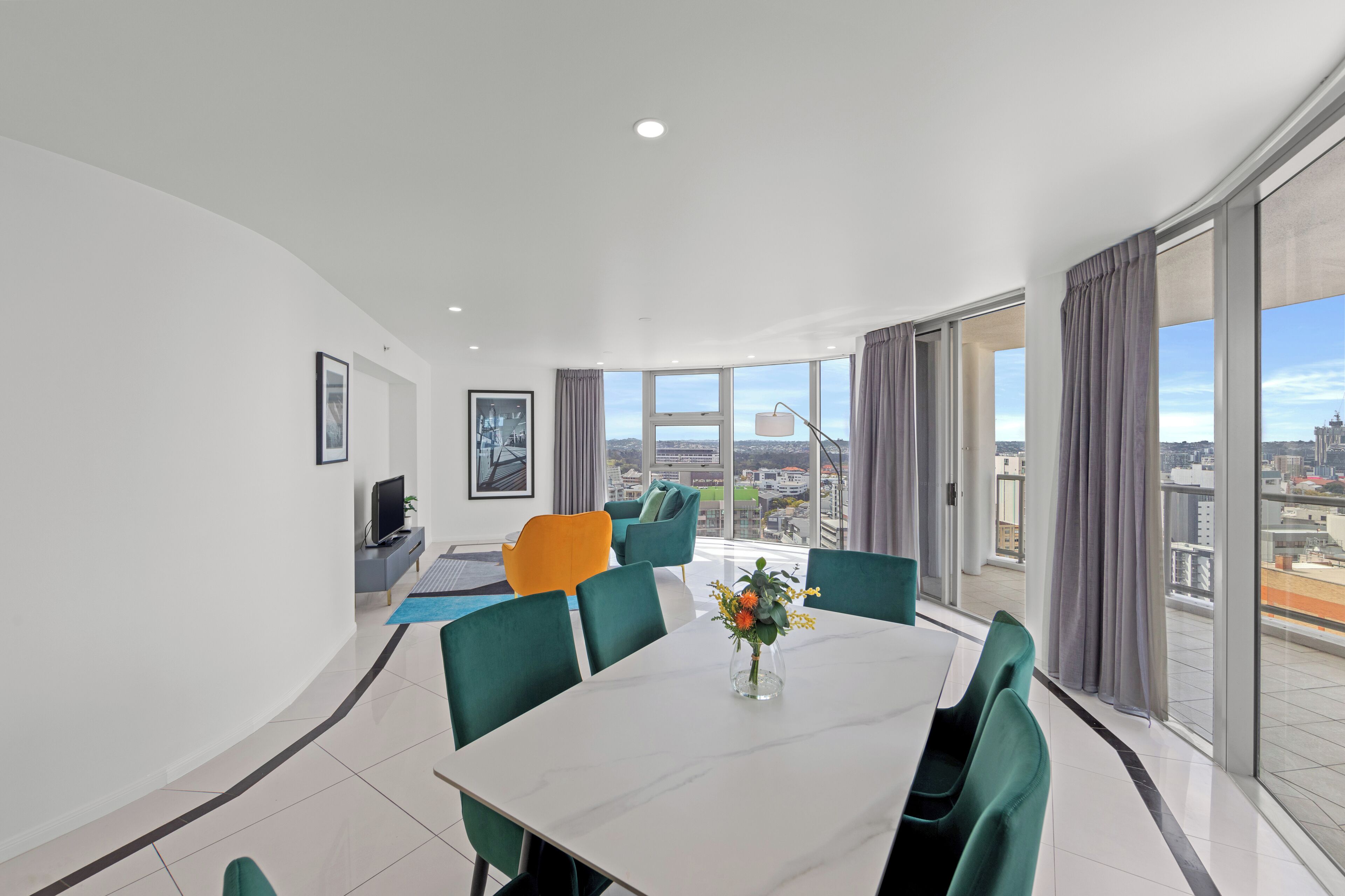 A modern dining area with a white table, green chairs, and a vase of flowers.