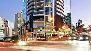 A tall, modern hotel with a curved facade, multiple balconies, and a prominent entrance area with lighting. - CLLIX Brisbane Central Apartments (Brisbane)