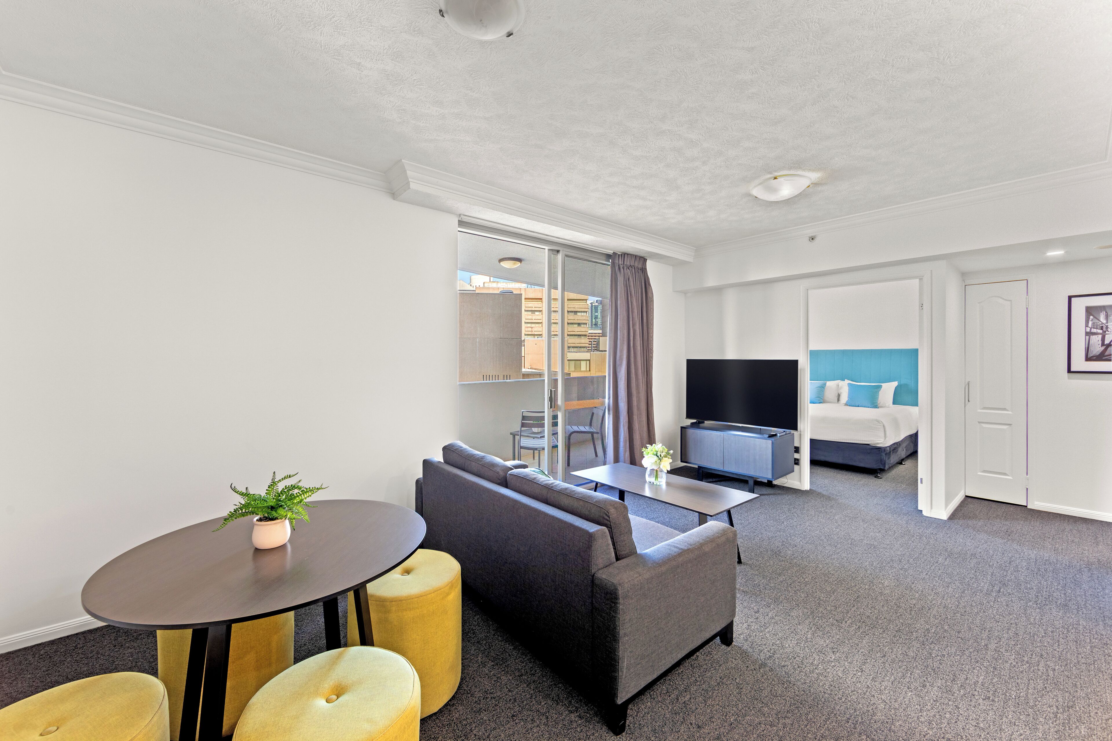 Una habitación de hotel moderna con sofá, una mesita con una planta, televisor y cama con una pared de acento azul.