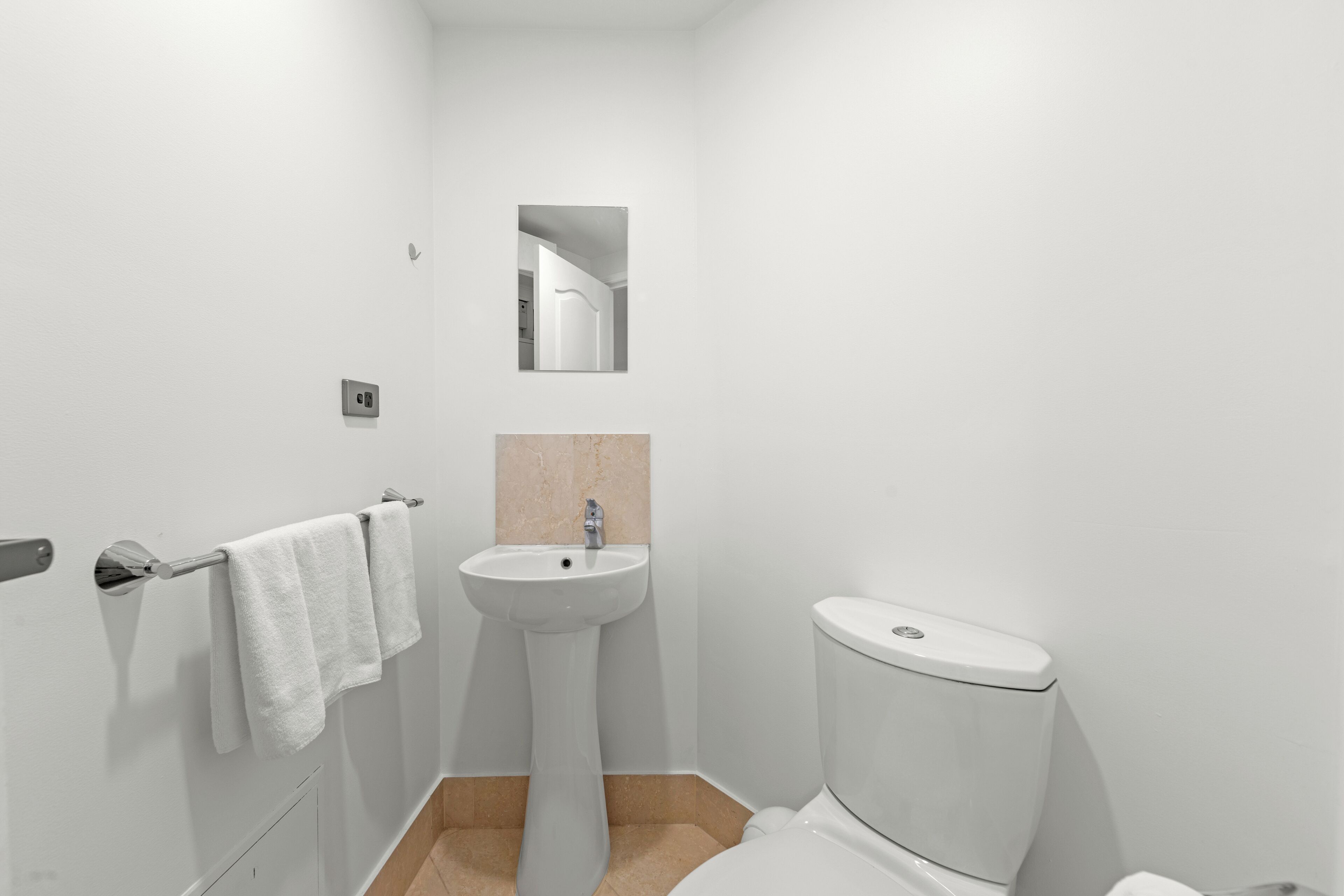 Um banheiro pequeno e moderno, com pia, vaso sanitário e porta-toalhas brancos.