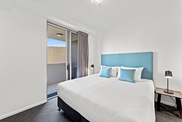A hotel room with a large bed, a blue headboard, and a nightstand with a lamp. - CLLIX Brisbane Central Apartments (Brisbane)