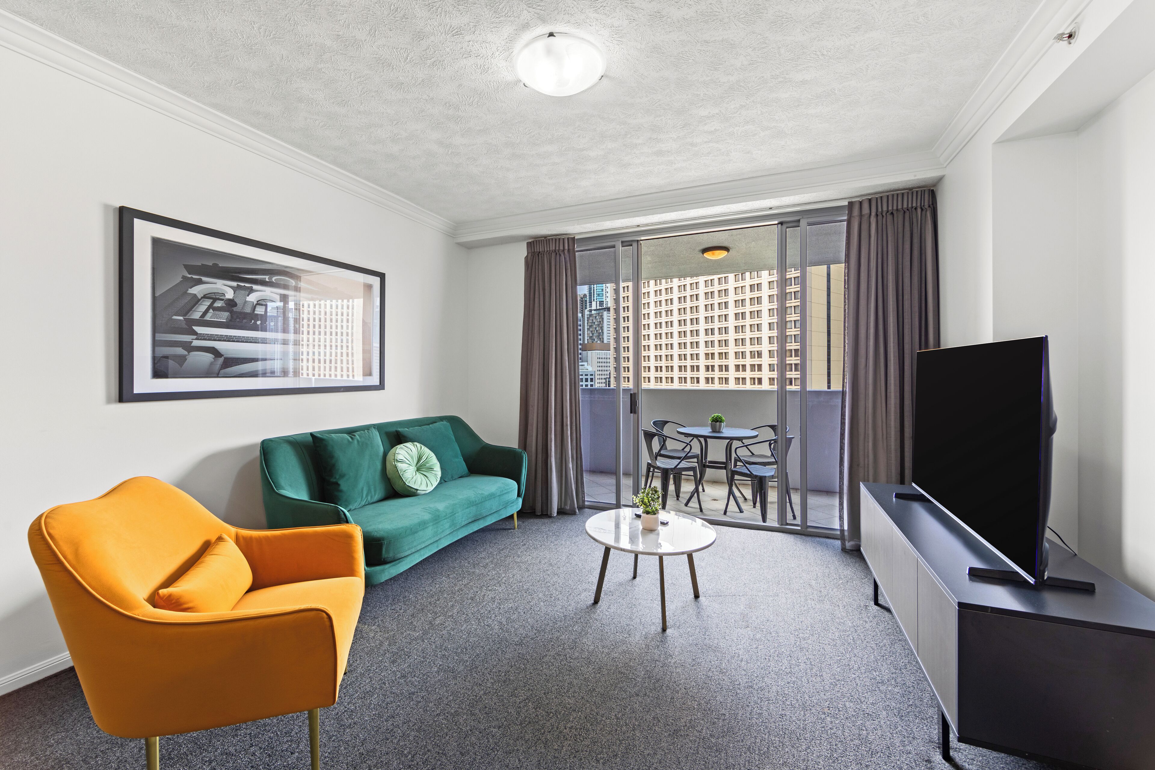 Una habitación de hotel moderna con sofá, sillón, televisión y balcón con vista a la ciudad.