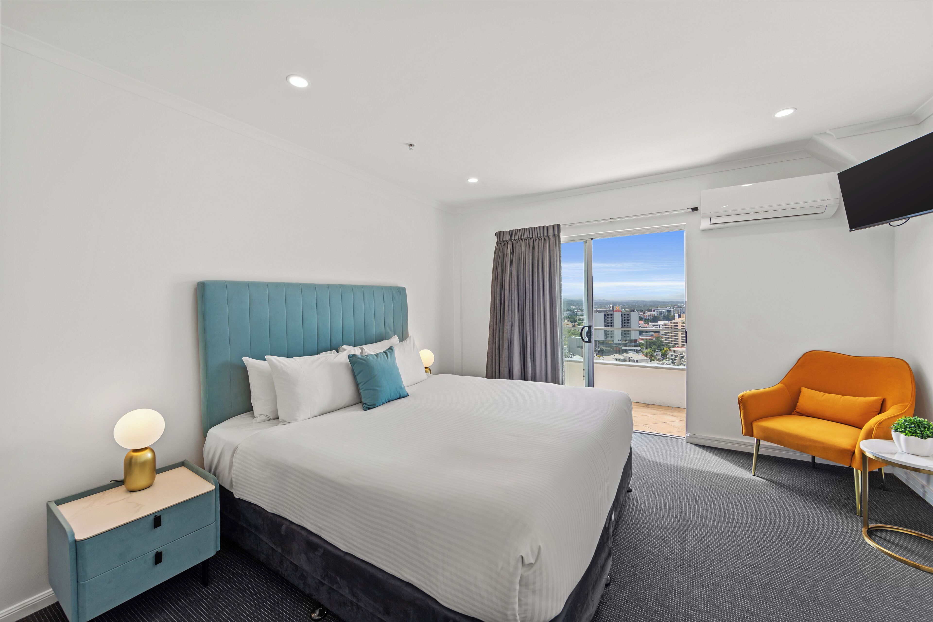 Habitación de hotel moderna con una cama grande, una mesita de noche, una silla y vistas a la ciudad.