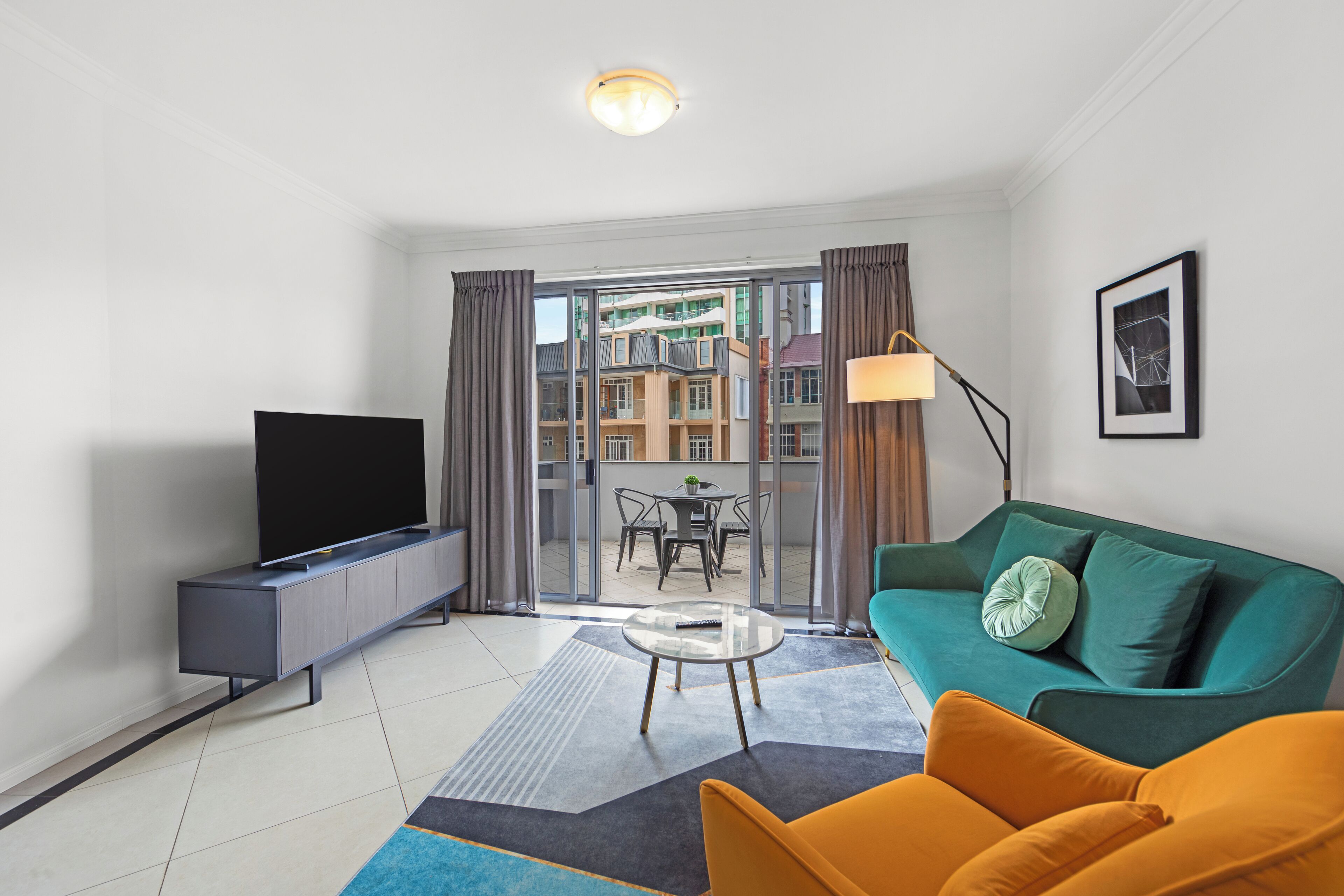 Een moderne woonkamer met een flatscreen televisie, een groene bank, een gele fauteuil en een glazen salontafel.