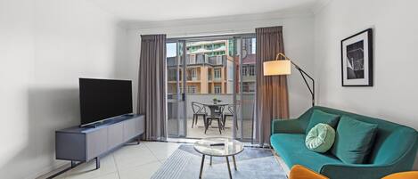Een moderne woonkamer met een flatscreen televisie, een groene bank, een gele fauteuil en een glazen salontafel.