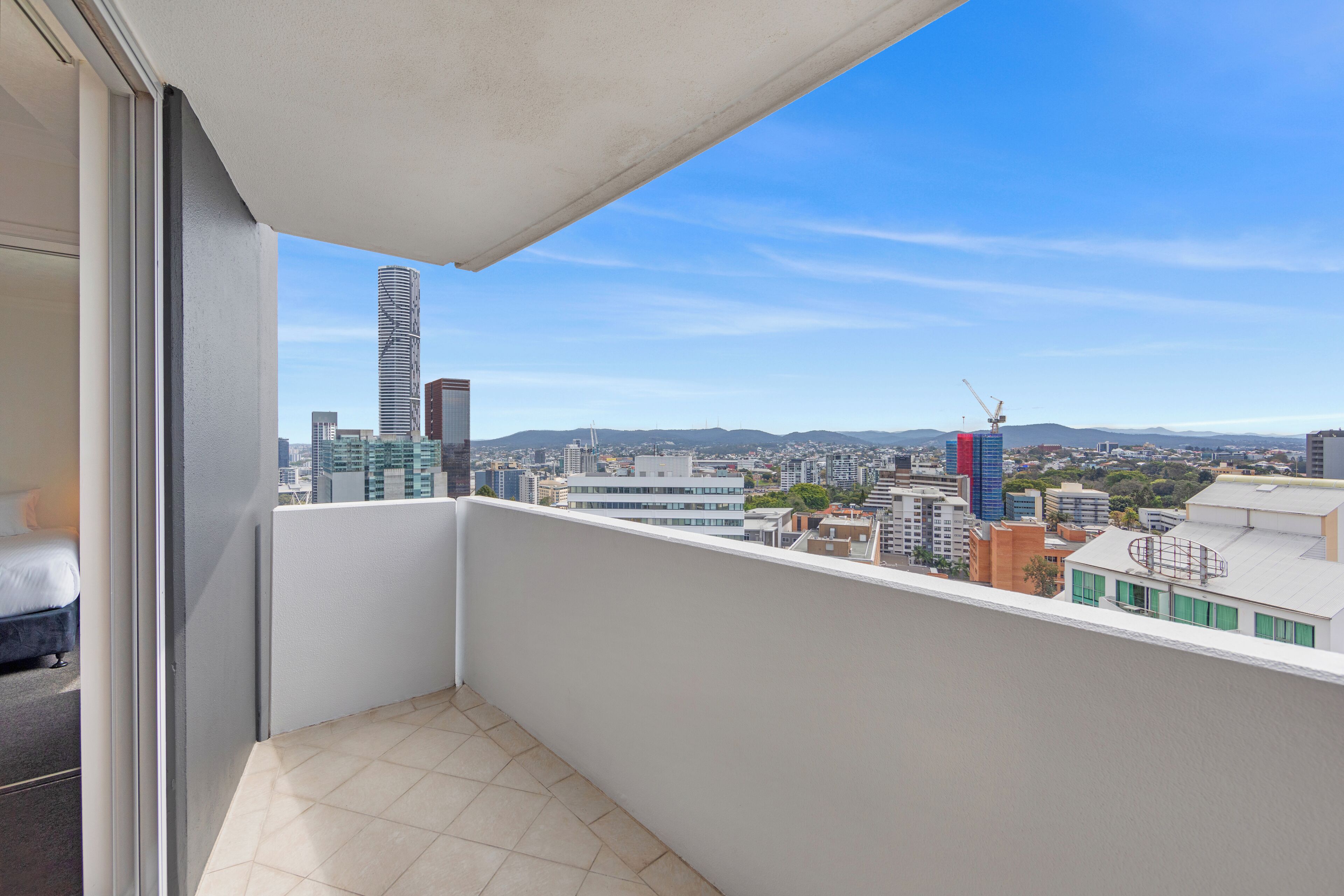 A balcony with a city view, including a tall building and construction cranes.