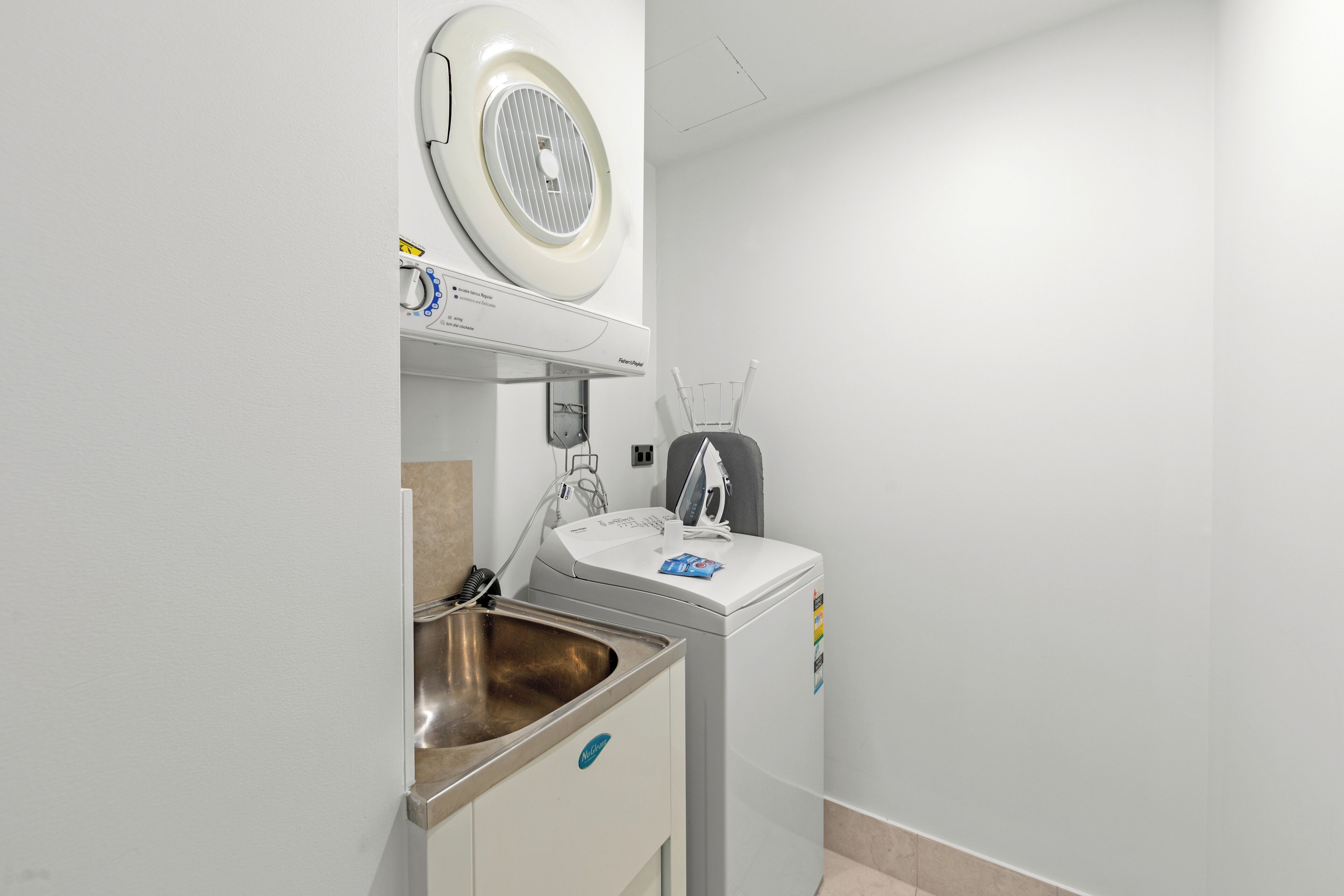 Een kleine badkamer met een wastafel, een wasmachine en een plafondventilator.
