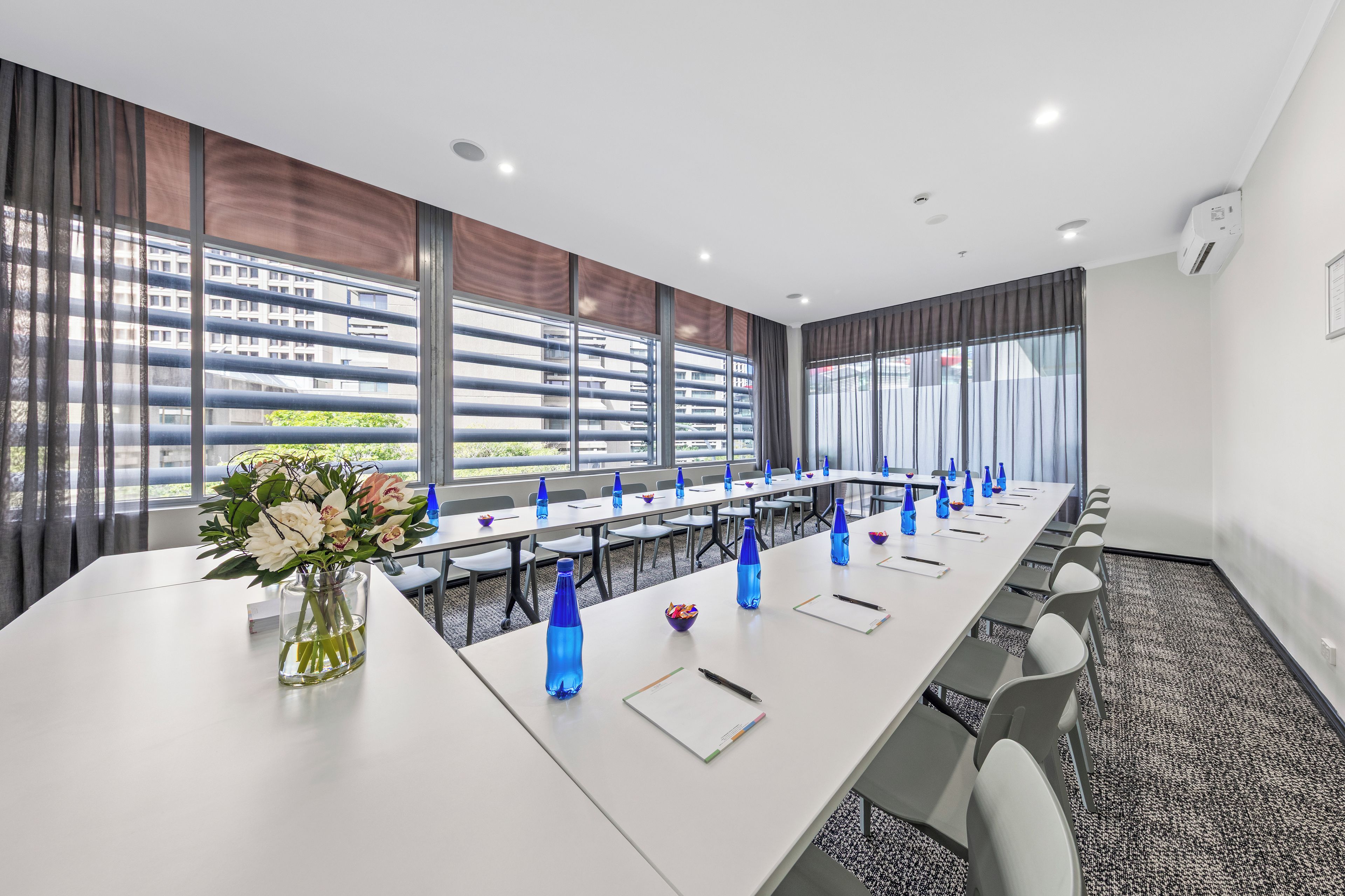 Un salón de conferencias con una larga mesa, sillas y un jarrón de flores.