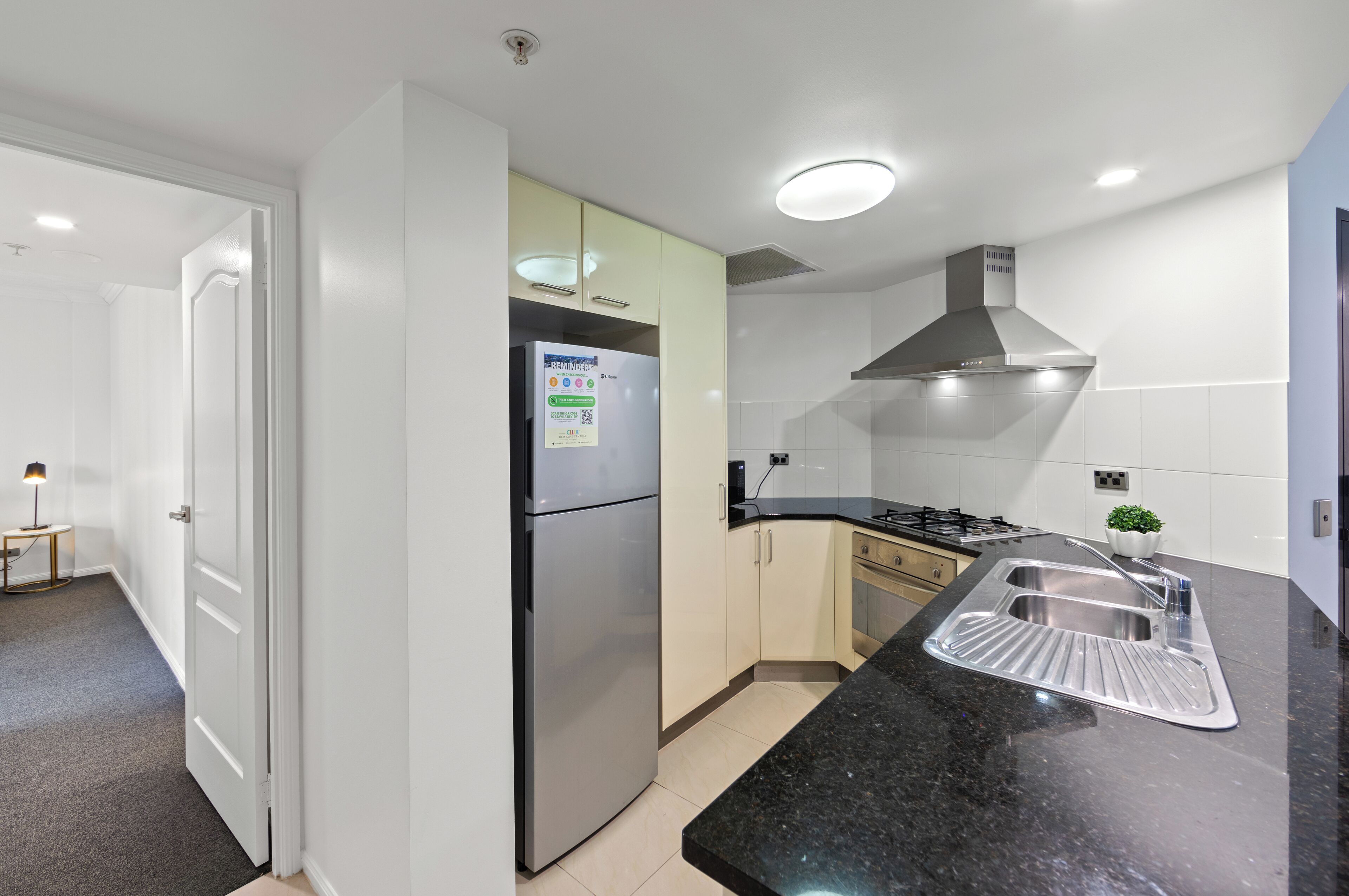 A modern kitchen with a stainless steel refrigerator, a black granite countertop, and a stainless steel sink.