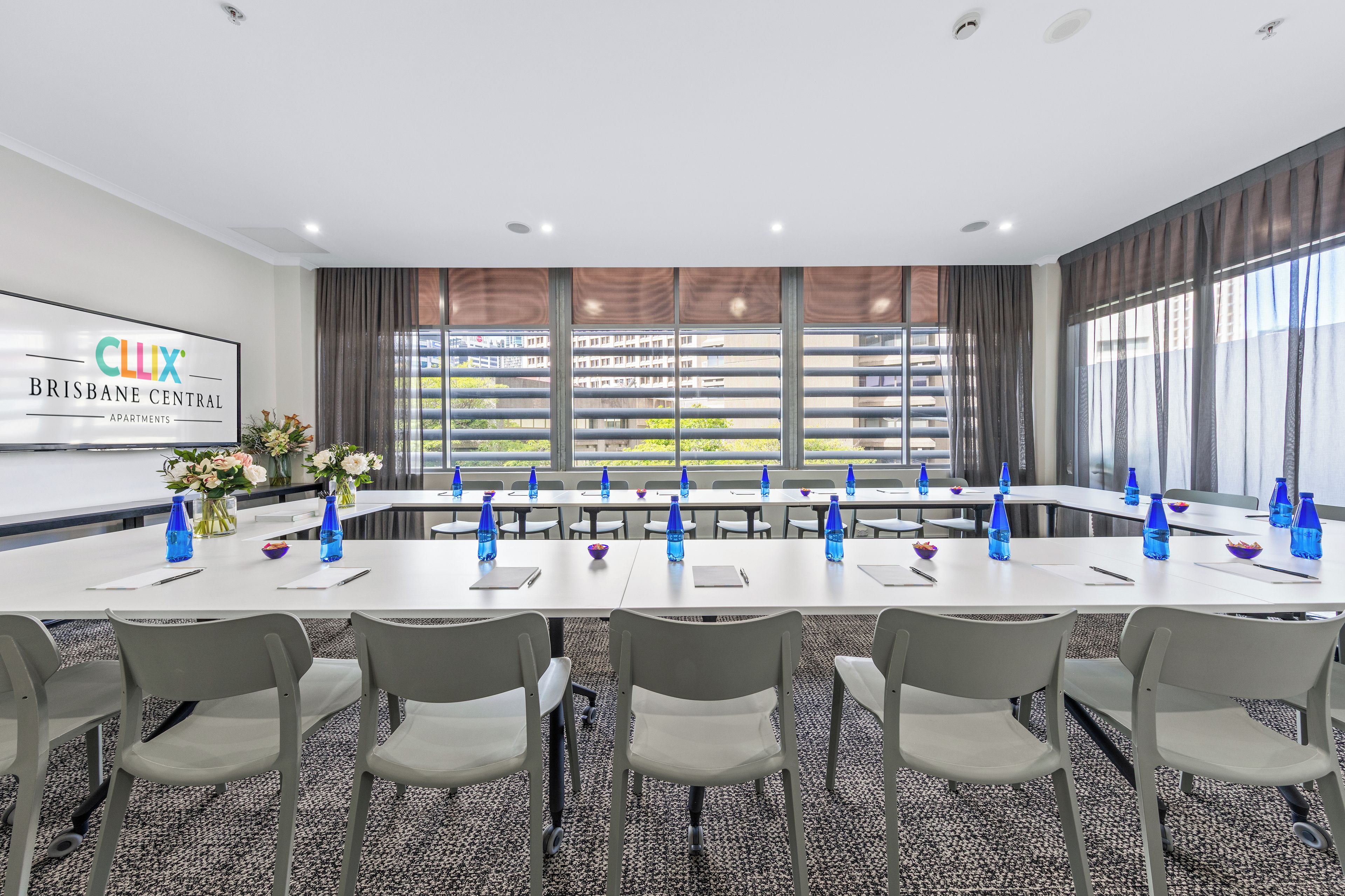 A conference room with a long table, chairs, and a large window with blinds.