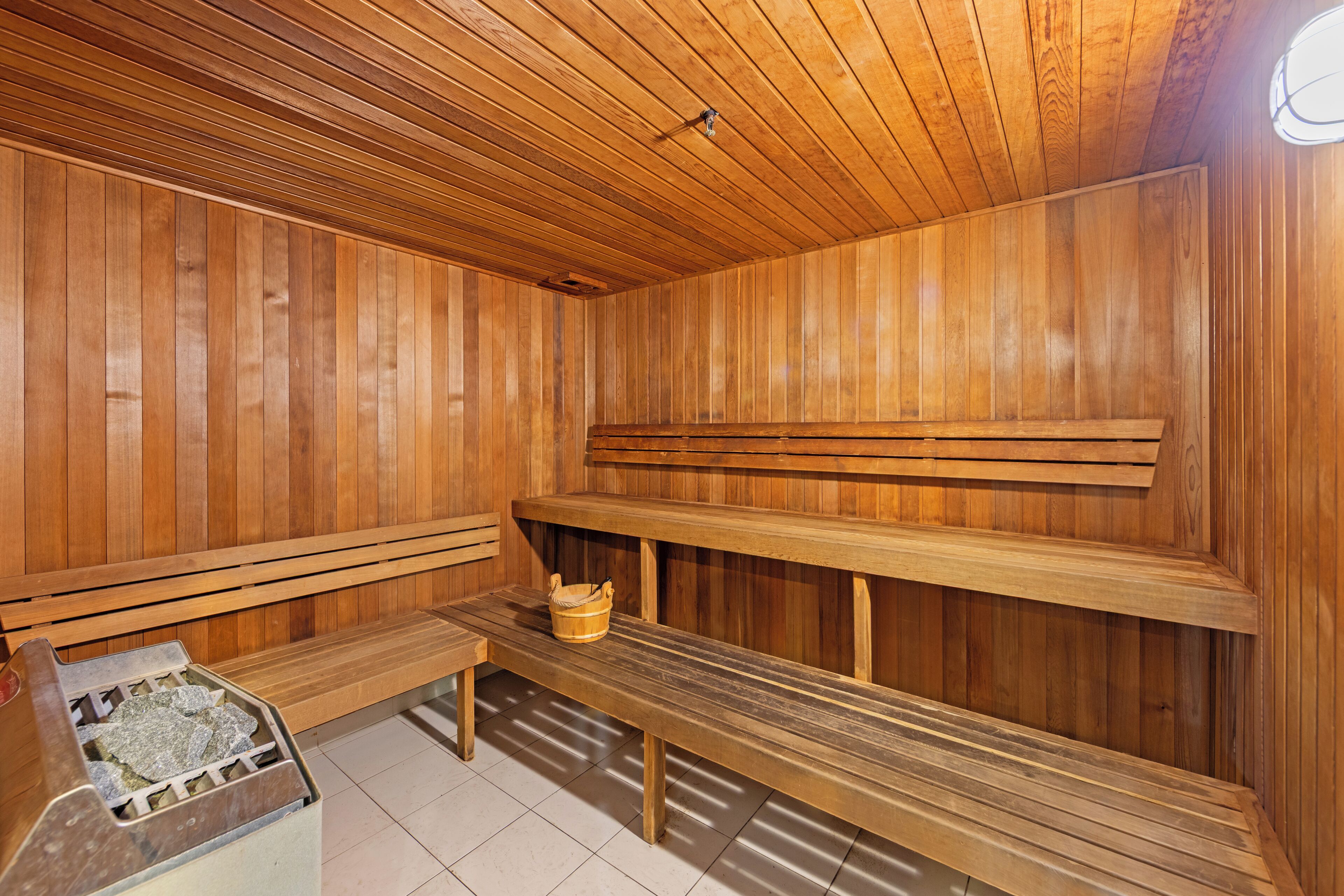 Una sauna con bancos de madera y un asiento con un balde.