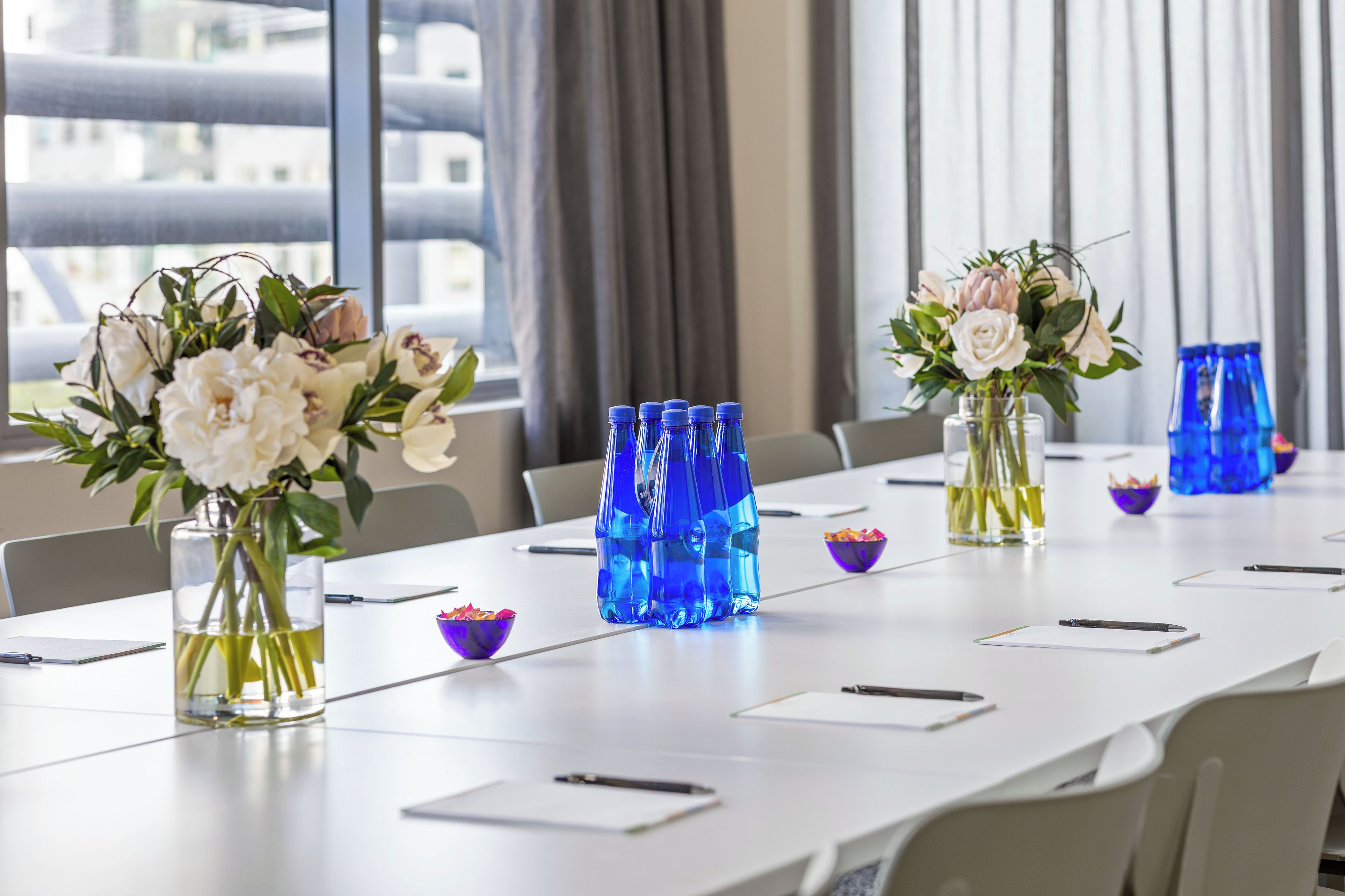 Una mesa de conferencias con jarrones de flores y botellas de agua azules.