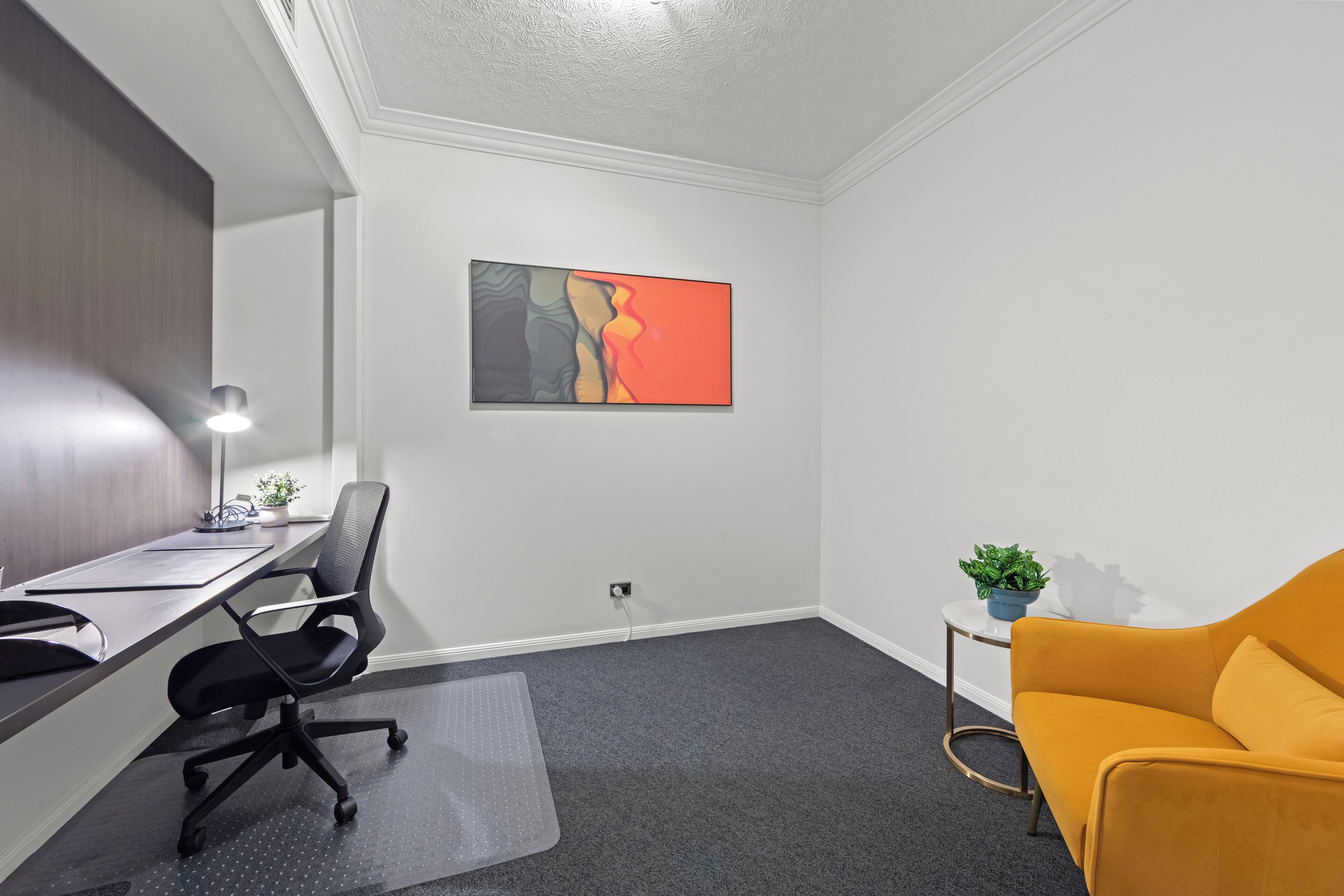 A modern office space with a desk, office chair, and a yellow sofa.