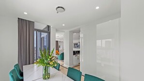 A modern dining area with a white marble table, teal chairs, and a vase with flowers. - CLLIX Brisbane Central Apartments (Brisbane)
