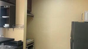 Une cuisine équipée d’une cuisinière, d’un four et d’un réfrigérateur. On y trouve un évier et un égouttoir à vaisselle. Les murs sont de couleur beige et le sol est carrelé.