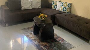 Un salon avec un canapé marron, une table basse sur laquelle est posé un vase de fleurs, un tapis à motifs, une horloge et un tableau encadré au mur.