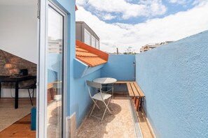 Une petite terrasse extérieure avec une table et des chaises, un mur bleu et un toit rouge.