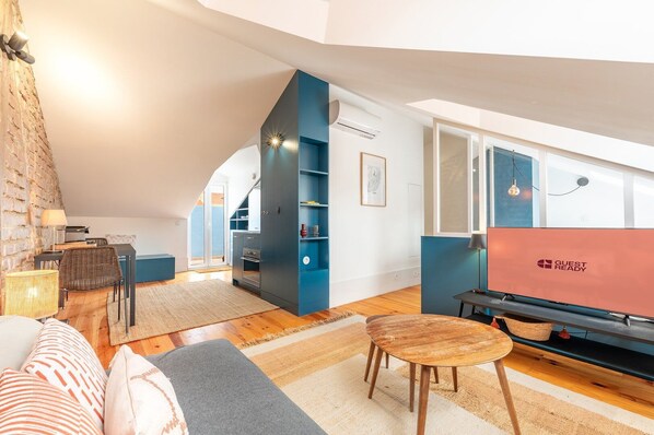 Un salon moderne avec un plafond de style industriel, un coin repas et une cuisine dotée de meubles bleus.