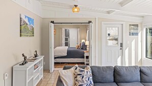 Une pièce comprenant un lit, un canapé, une console blanche et une porte donnant sur une autre pièce.