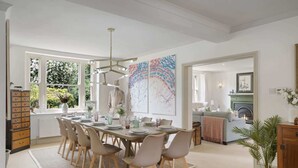 Een eetkamer met een grote tafel gedekt voor zes personen, omringd door zes stoelen. Er is een groot raam met uitzicht op groen buiten.