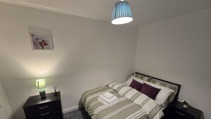 Ein Schlafzimmer mit einem Bett, Nachttischen, einer Lampe, einer Pendelleuchte und einem Bild an der Wand.