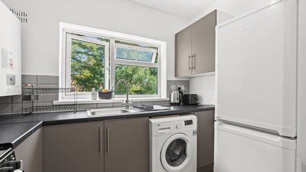 Eine moderne Küche mit eingebauter Waschmaschine und Trockner, einem großen Fenster mit Blick auf Grünflächen und einer Spüle aus Edelstahl.