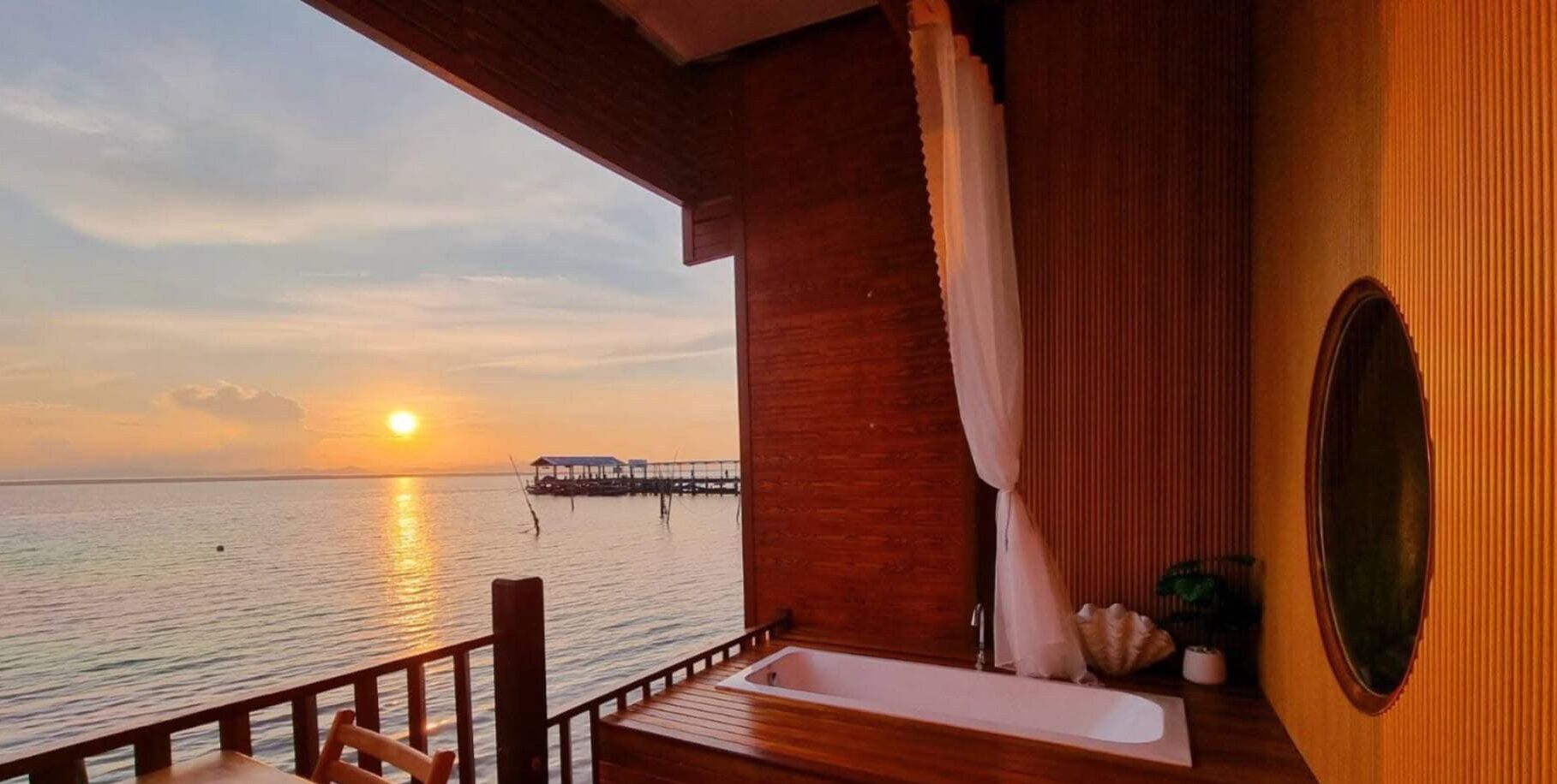 Een balkon met uitzicht op de ondergaande zon boven de zee, een houten terras en een bad.