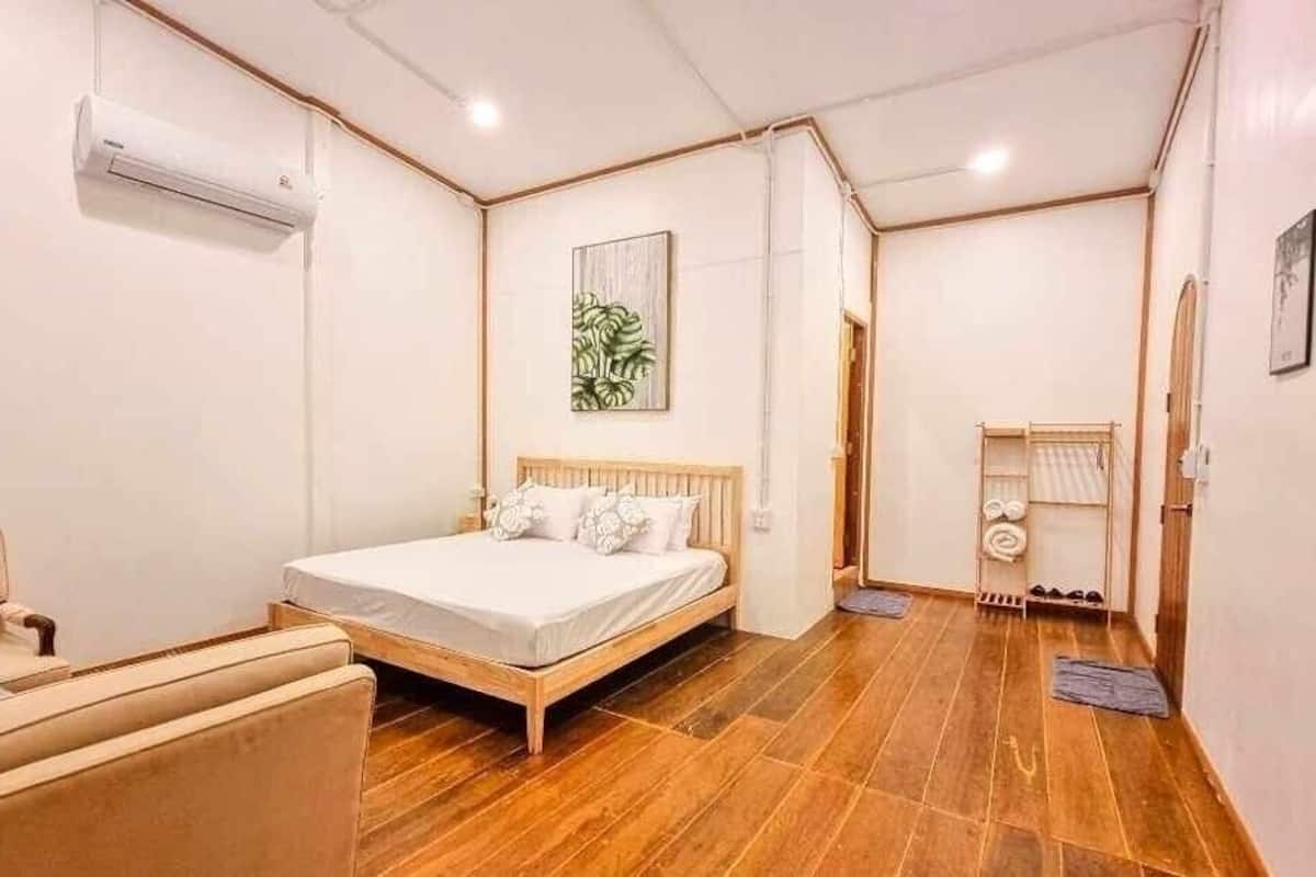 A bedroom with a bed, a chair, an air conditioning unit, and a small table with a towel rack.