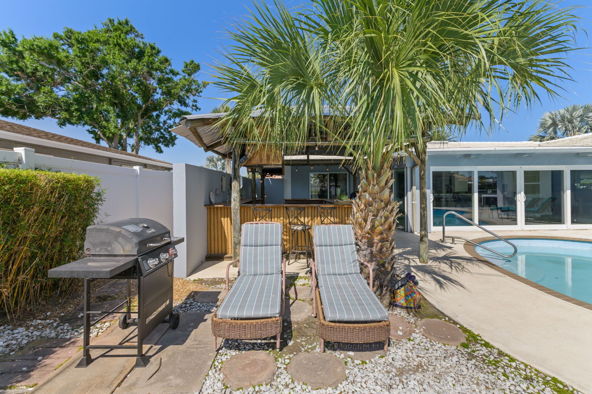 A poolside area with two lounge chairs, a barbecue grill, and a palm tree.