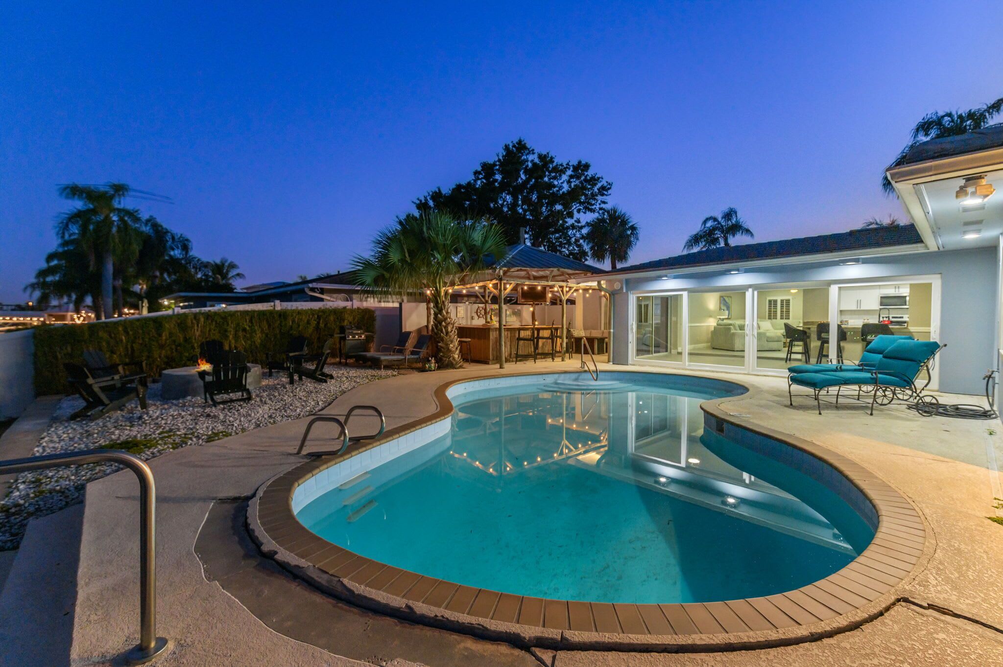 A swimming pool with a curved design, surrounded by a patio area with lounge chairs and a barbecue setup.