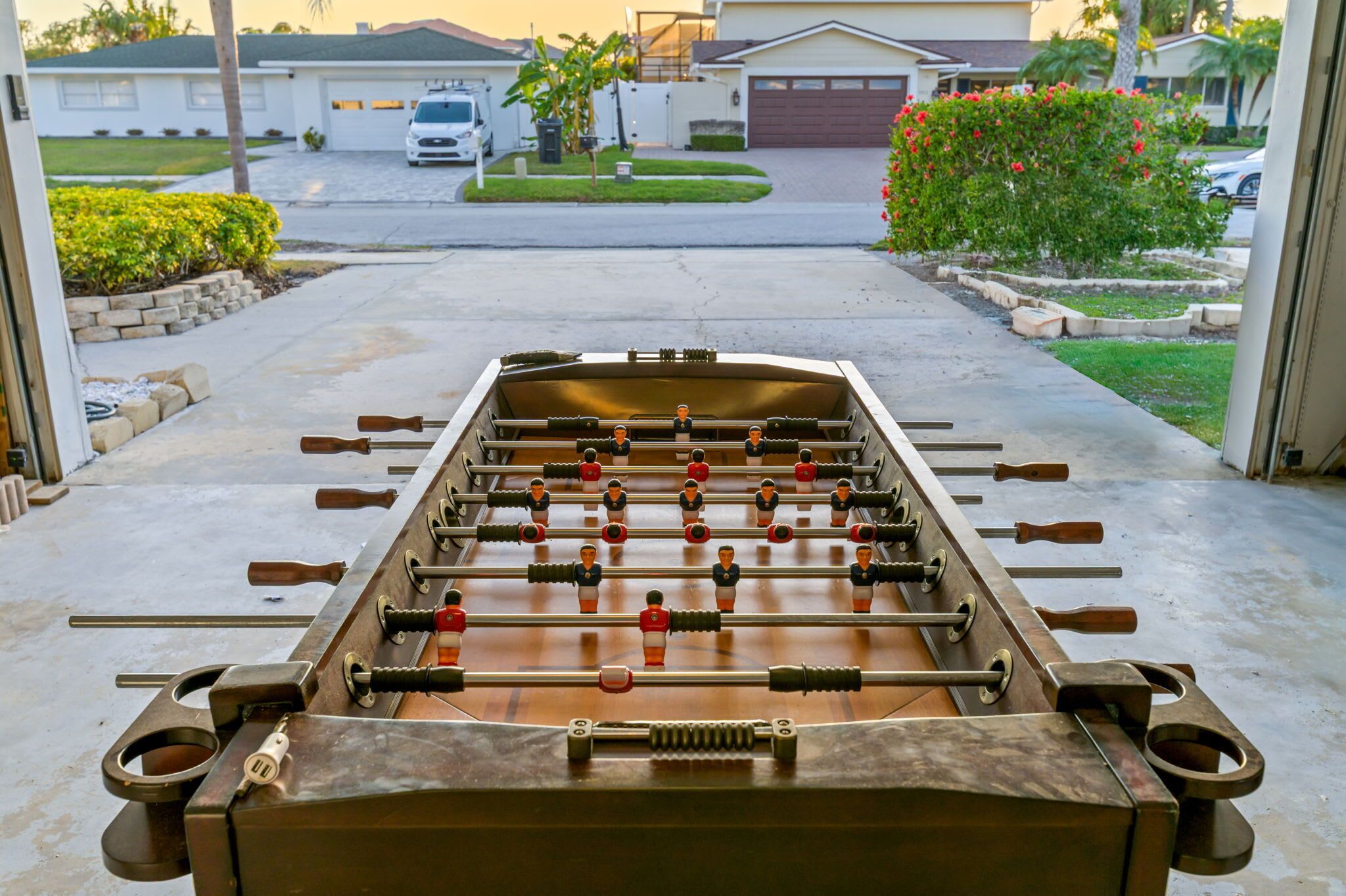 A foosball table in a garage with a view of a residential street and houses in the background.