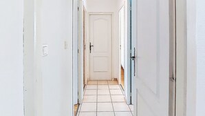 Kapea käytävä, jonka seinät ovat valkoiset ja jossa on laattalattia, johtaa käytävän päässä olevaan oveen.