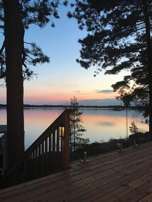 Une terrasse en bois donnant sur un lac paisible, avec un coucher de soleil en arrière-plan.
