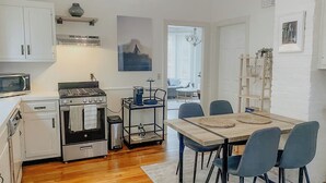 A compact kitchen with a stove, microwave, and oven. There is a dining table with chairs and a chandelier above. - Charming 2-bedroom house super close to Brown & RISD, Wayland Square (Providence)