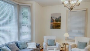 A living room with a grey sofa, two white armchairs, a round coffee table, and a chandelier. - Charming 2-bedroom house super close to Brown & RISD, Wayland Square (Providence)