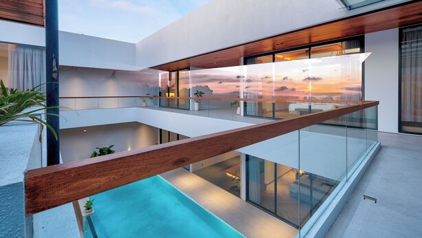 Um edifício moderno com varanda de vidro com vista para uma piscina e um pôr do sol.