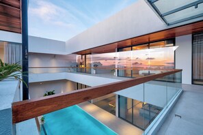 Um edifício moderno com varanda de vidro com vista para uma piscina e um pôr do sol.