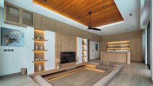 Uma sala de estar moderna com um amplo sofá modular, estantes embutidas, uma TV de tela plana e teto de madeira.