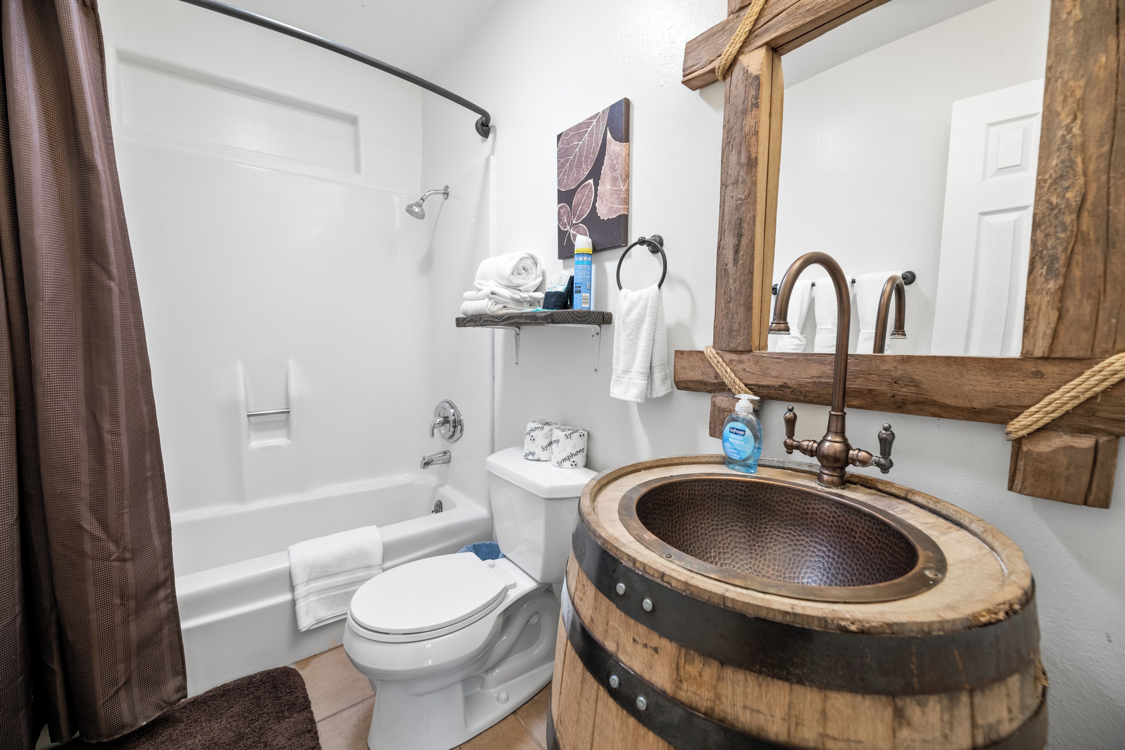 A bathroom with a bathtub, toilet, and sink with a wooden barrel.