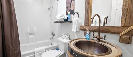 A bathroom with a bathtub, toilet, and sink with a wooden barrel.