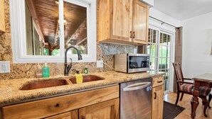A kitchen with granite countertops, wooden cabinets, a stainless steel dishwasher, and a microwave. - Moonlight Serenity (Big Bear Lake)